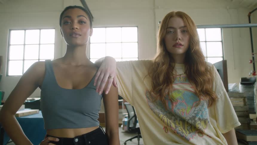 A pair of young women look into the camera as they pose together in a storage room