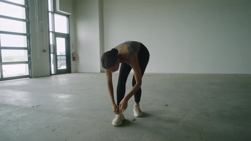 Woman in athletic clothing tying her shoes in a large empty garage