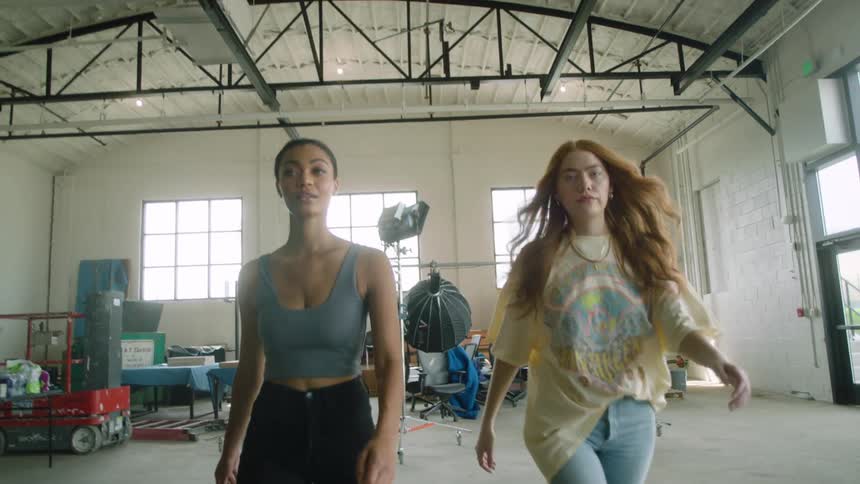 A black and white woman walking like models towards the camera in a building