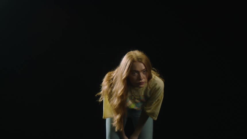 Young blonde woman standing in a dark room whipping her long hair looking at the camera