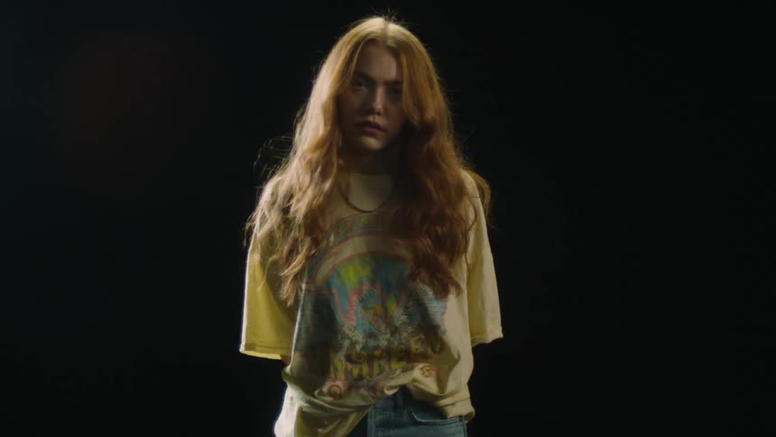 A woman with a t shirt and jeans standing and staring with a black background