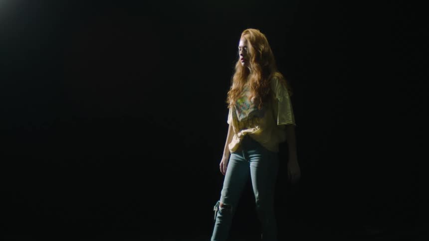 Woman with long hair rubs her arm then swings her arms while standing in a dark area