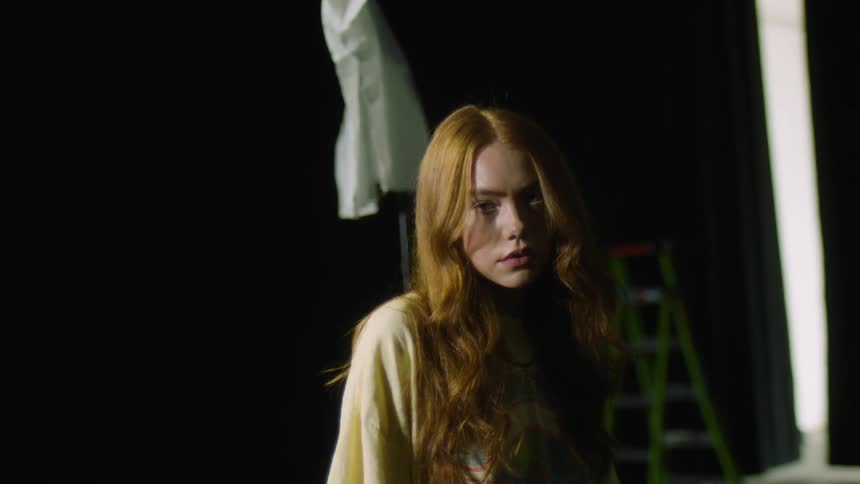 A redheaded girls is on stage in front of black curtains stepping to her right