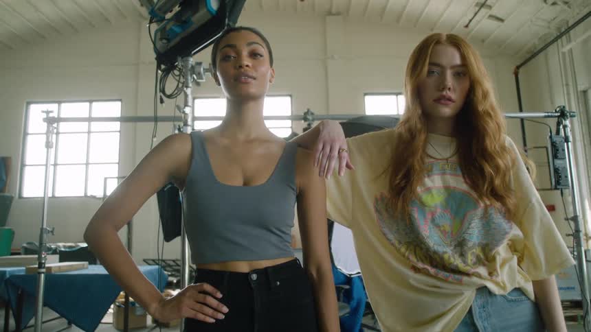 Woman with long hair rests her arm on the shoulder of another woman as they stand in a studio with audio equipment
