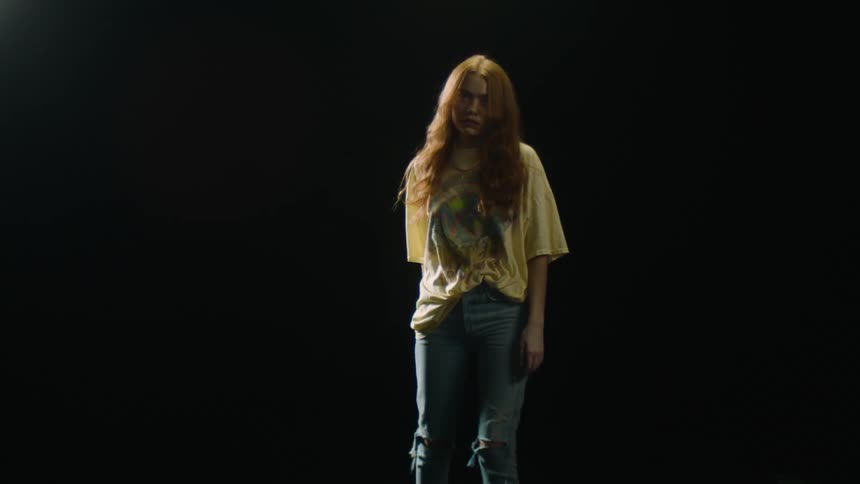 A teenage girl standing in a dark room swinging her arm around