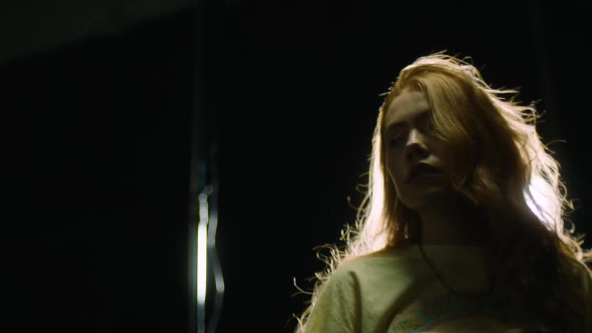 A young woman walks under a spotlight in a dark studio