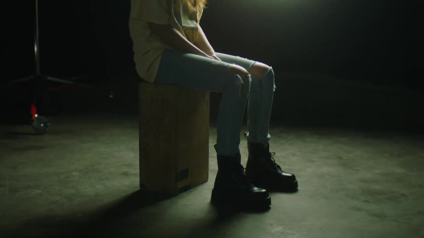 A young woman sits on a wooden box in front of a spotlight in a photography studio