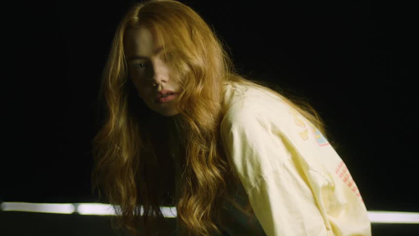 A young woman with long red hair poses in a dark studio