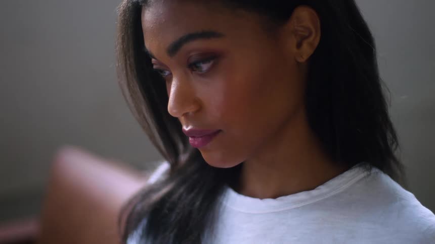 A young black woman in a white tee shirt sits in a chair as shes reading
