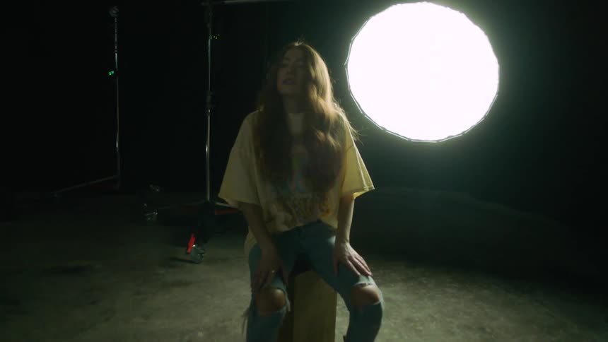 A young woman with long hair sits down on a concrete block in a photography studio set up in a garage