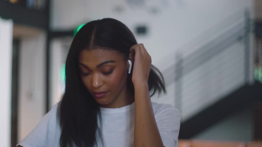 Black woman with an ear pod in her ear pushes her hair behind her ear with her hand