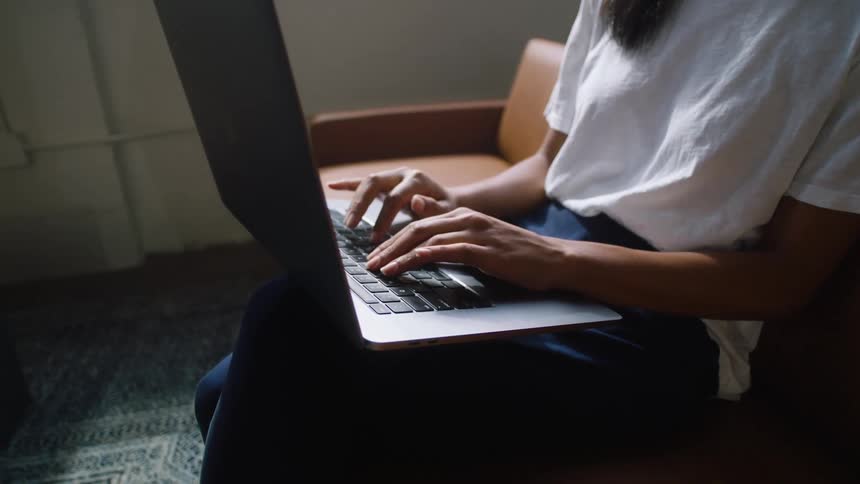 Woman sitting on a chair in a room types on a laptop