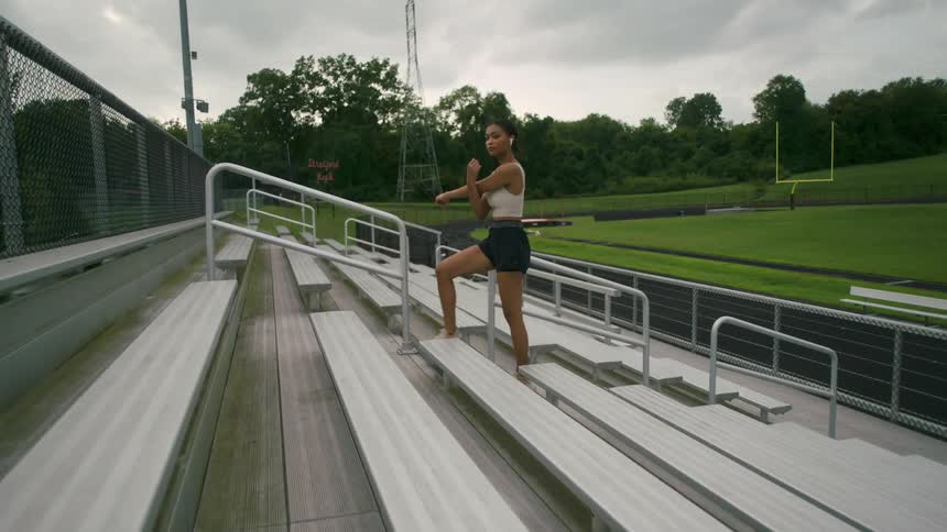 A woman is walking up a st of bleachers and stretching