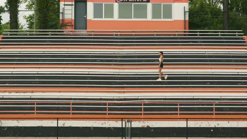 A woman walks on a stadium bench and comes to a stop