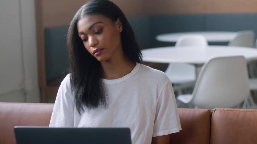 A woman sits on a couch while she uses a laptop