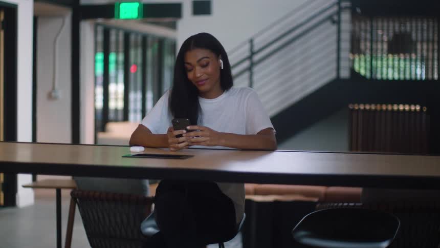 A woman sits in a building and scrolls on her cell phone