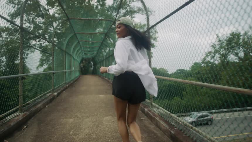 A teenage girl glances over her shoulder as she runs across a bridge over a street with cars driving