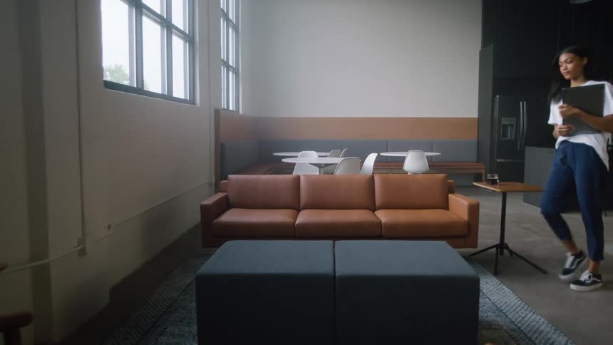 A woman with a laptop walking up to and sitting on a couch