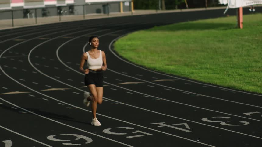 A woman runs on a track while wearing headphones
