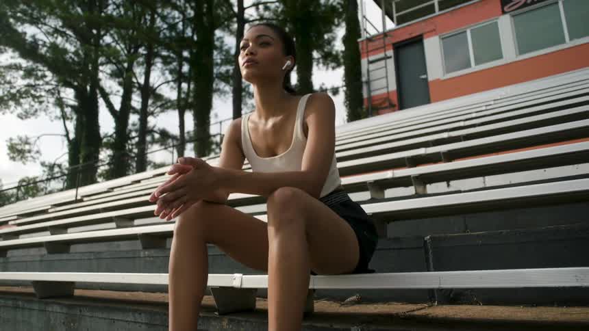 Woman wearing shorts and a tank top sits on the bleachers in front of a building