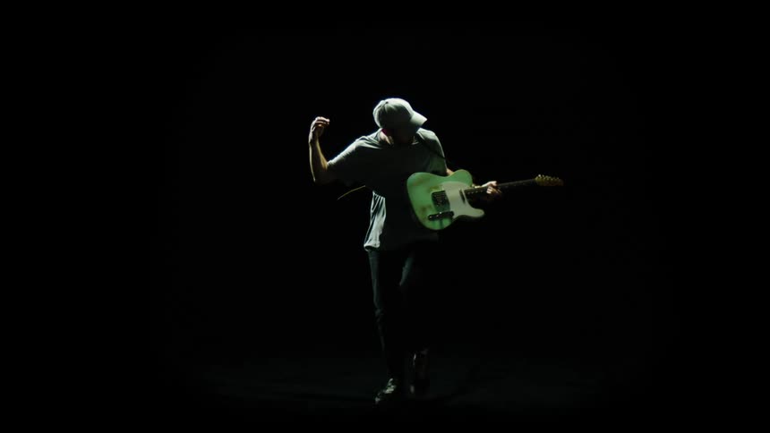 Man playing his guitar enthusiastically in a dark room