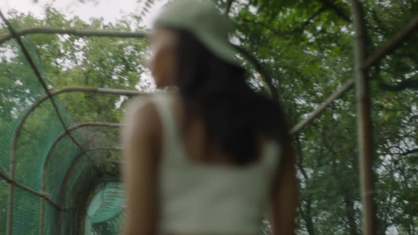 A woman walking down a fenced walkway looks over her shoulder to glance at the camera before continuing on her way
