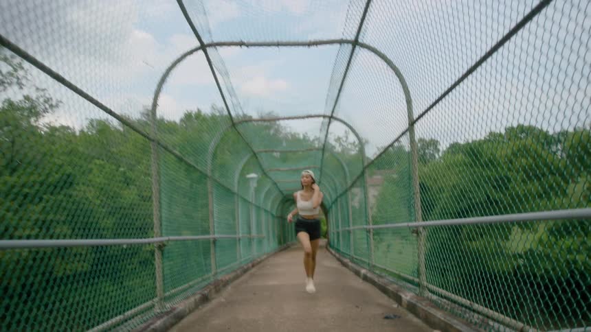 A female running in the woods on a fenced in bridge
