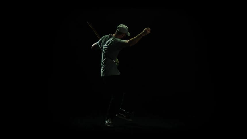 A man with a hat playing a guitar with lights flashing and a black background