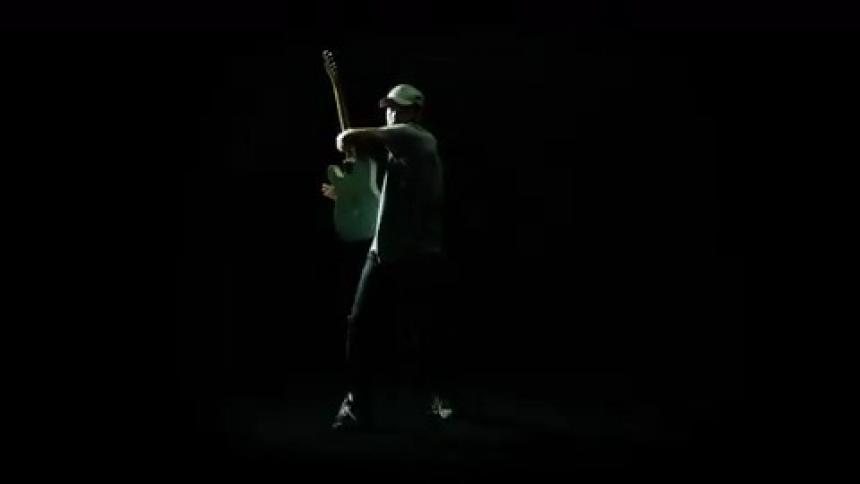 A man plays his guitar in front of a strobe light