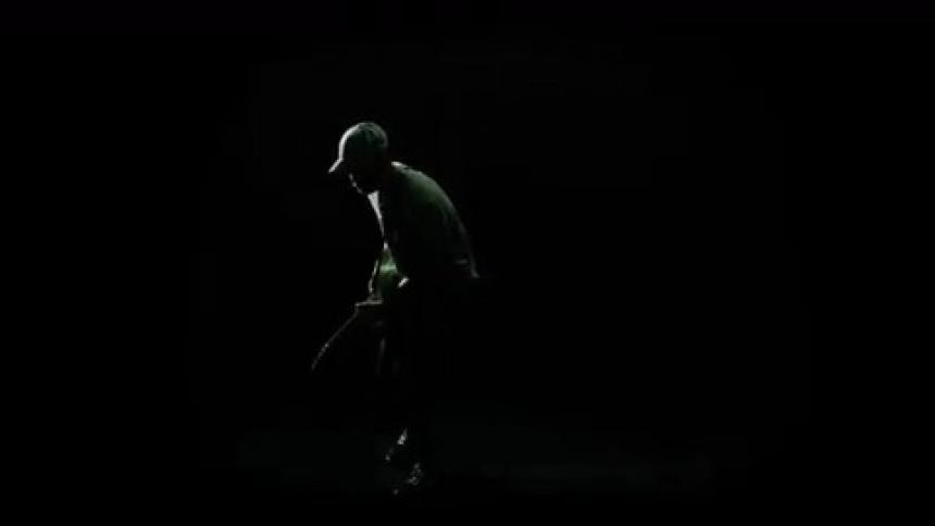 A man with a hat playing a guitar with lights flashing and a black background