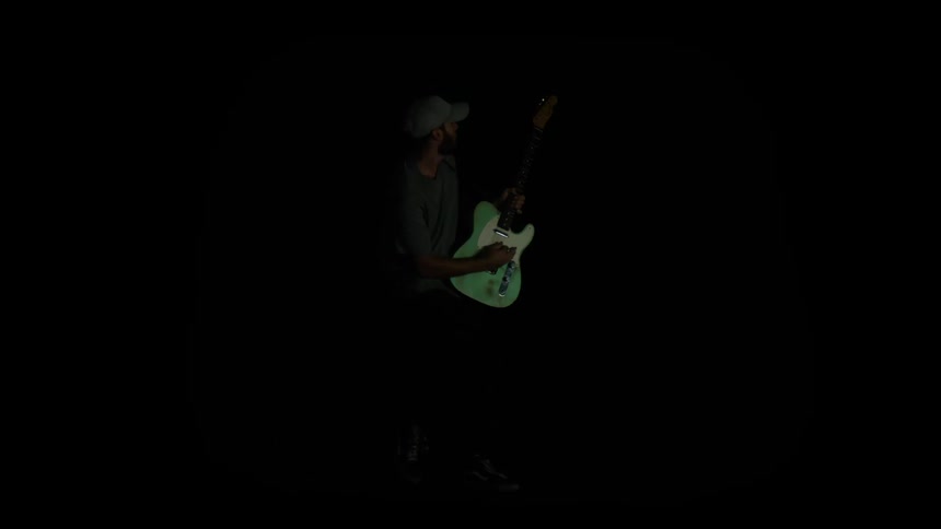 A male holds a white guitar in poses on an unlit stage with strobing lights
