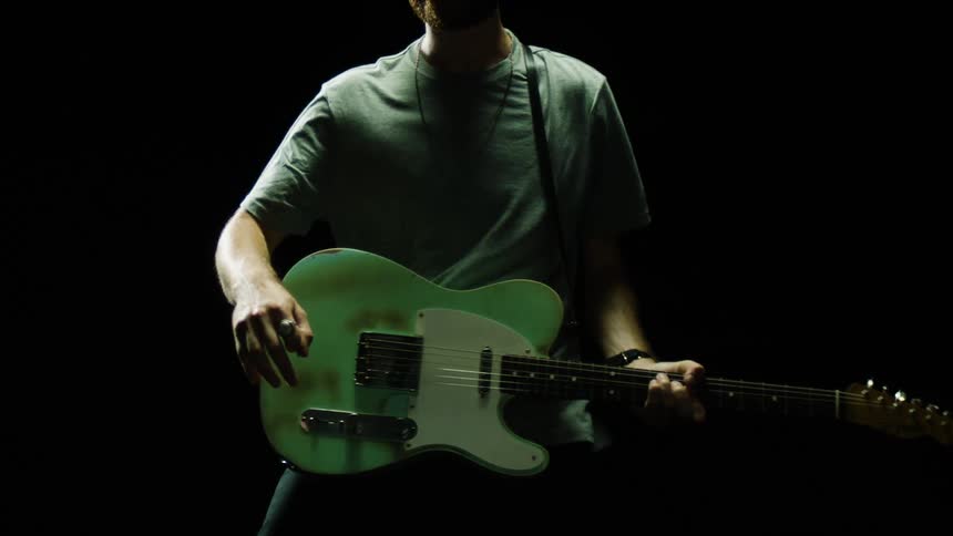 A man is playing and swinging his guitar