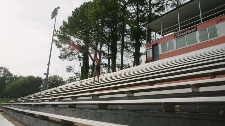 A teenage girl walks up stairs in a stadium and sits down