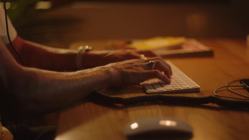 Person sitting at table listening to mobile phone types on computer keyboard