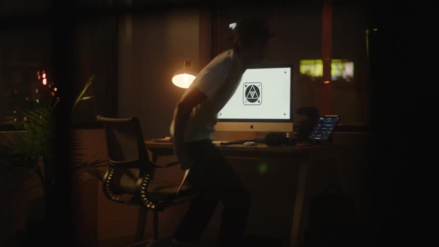 A teenage boys plays on his computer at home by a window as cars drive by and then jumps up from his chair and walks away