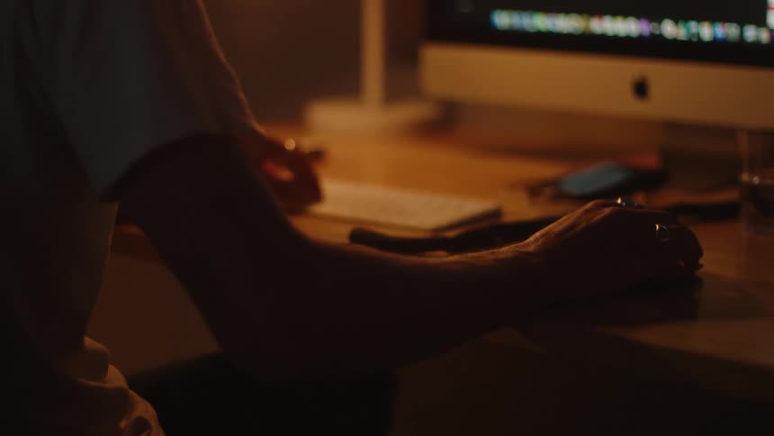 A person sits at a desk in front of a computer moving the mouse