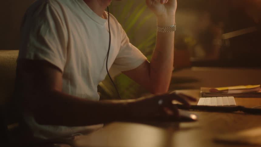 A man sitting at a desk and putting on headphones while using a mouse and keyboard