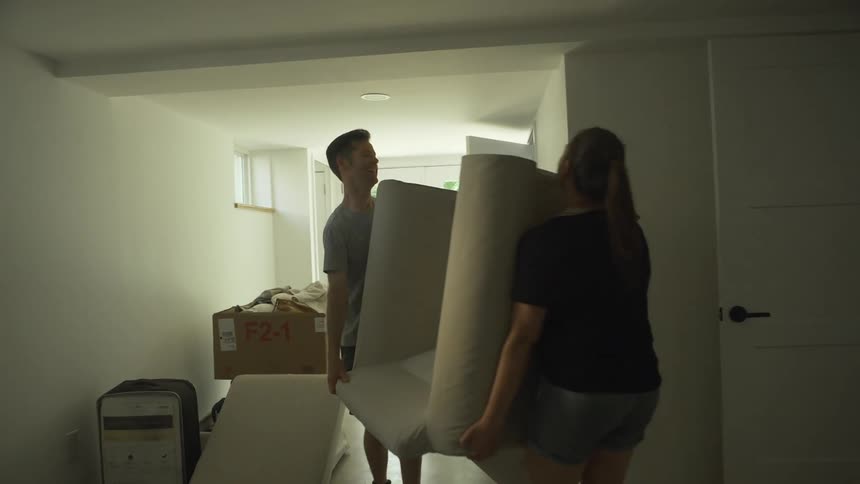 A young man and women laugh and smile as they carry a loveseat towards an open door