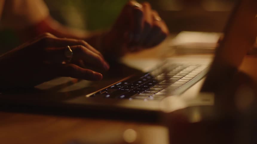 A woman typing on a laptop keyboard on a wood table