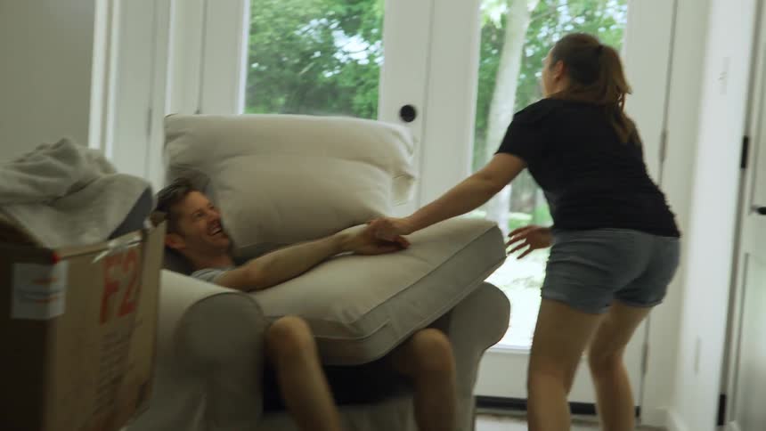 A woman and man play with the cushions of a chair before the woman stands begins to put them in their proper place