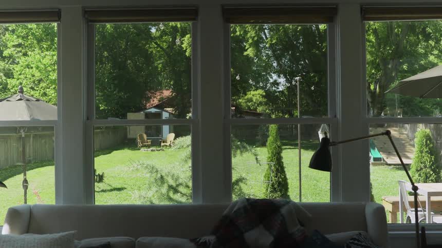 Man with a hat mowing the lawn in the fence lined backyard of a suburban house