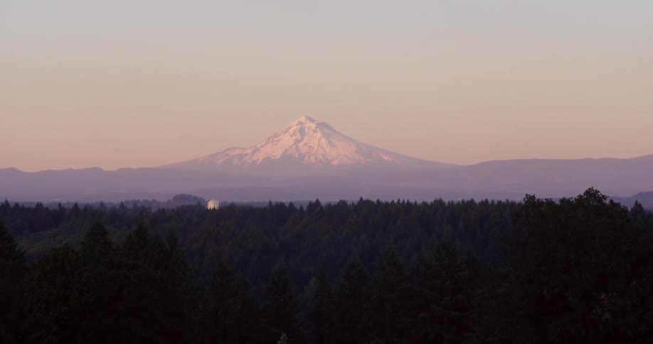 Wide shot of a snow covered mountain peak in the horizon at sunset