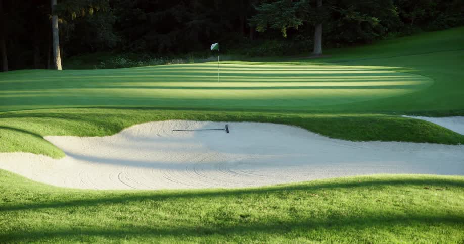Shadows fall across golf hole marked with flag on golfing green near sand trap
