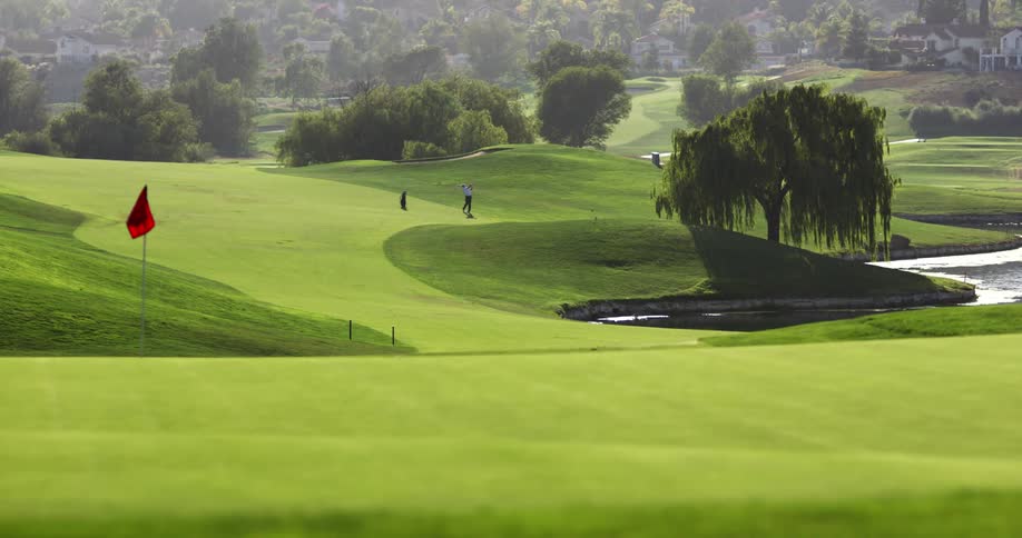 Golf course on a sunny day with trees and a red flag with a water feature