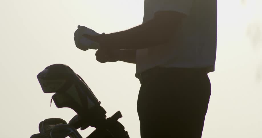 A man slips on a golf glove and tightens it near his clubs