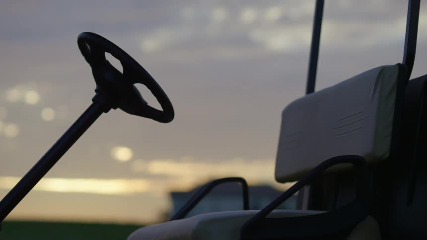 A golf cart sits in front of sun when it is low in the sky
