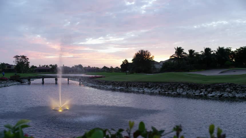 A golf course with a pond and fountain at dusk or dawn