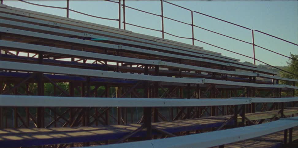 Empty metal bleachers at sunset or sunrise with some railing around the top and sides with trees in the distance