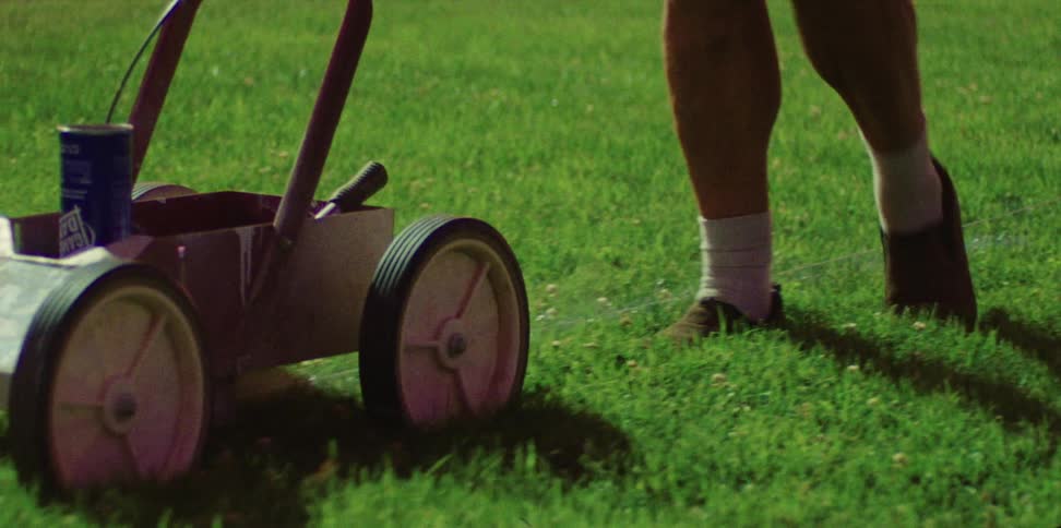 A man walking on grass pushing a cart
