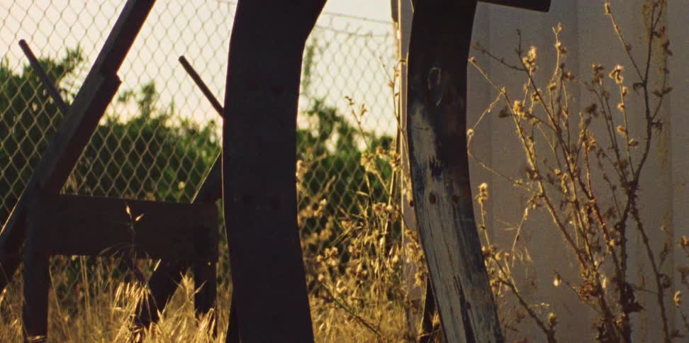 Rusted sports equipment against a chain link fence surrounded by weeds